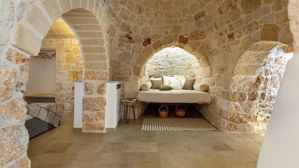 A cozy stone-walled room with a bed, a small table, and a radiator. - 2220 Trulli Biancapetra by Perle di Puglia (Francavilla Fontana)