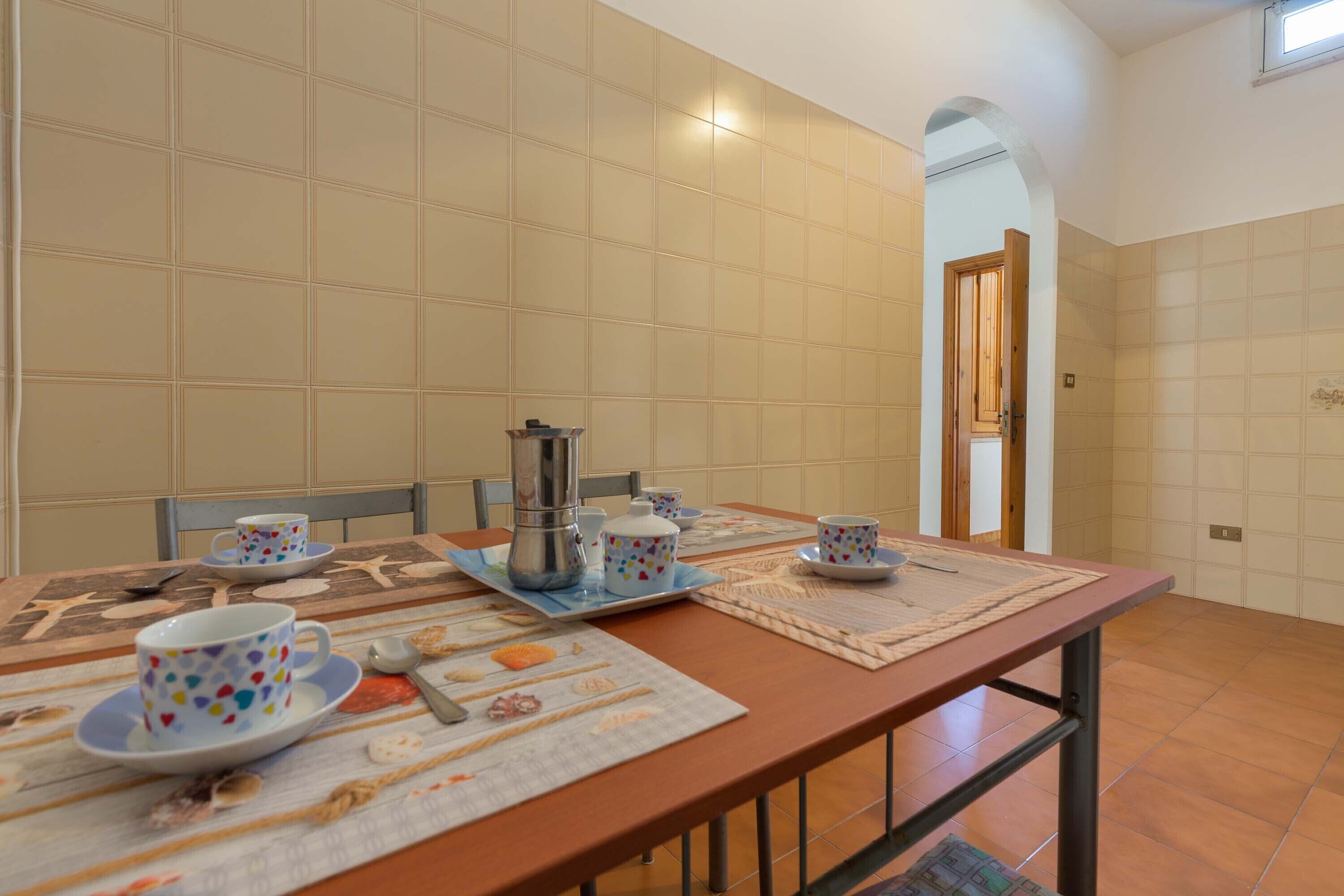 Een eethoek met een lange tafel gedekt voor twee personen, inclusief een koffiezetapparaat, kopjes en een placemat met afbeeldingen van eten.