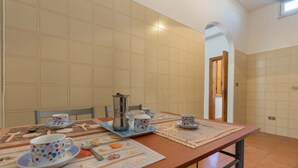 A dining area with a long table set for two, featuring a coffee maker, cups, and a placemat with food illustrations. - 2191 Appartamento Blue Dreams by Barbarhouse (Melendugno)