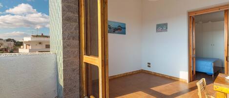 A room with a large window, a wooden door, a tiled floor, and a bed with a blue cover.