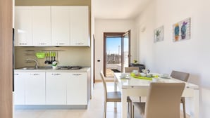 Une cuisine moderne avec des meubles blancs, un coin repas avec une table et des chaises blanches, et une vue à travers une porte ouverte.