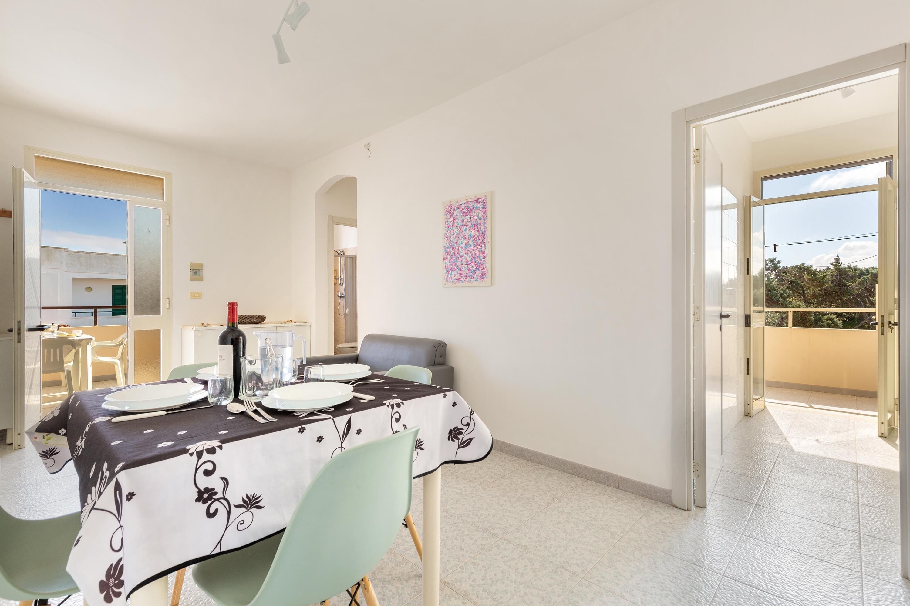 A dining area with a table set for four, a chair, a wine bottle, and a painting on the wall.