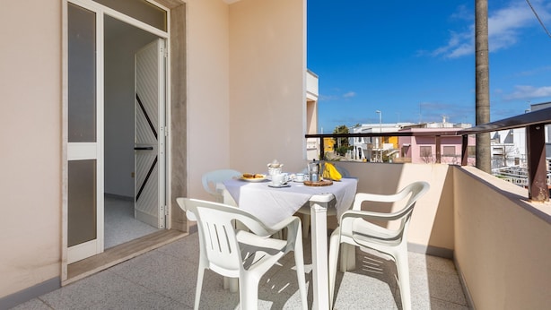 A balcony with a table set for two, chairs, and a view of buildings in the background. - 2226 Carlotta`s House by Barbarhouse (Melendugno)