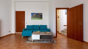 A living room with a teal sofa, a white cabinet, and a coffee table. There is a wooden door on the right and a picture on the wall. - 2253 Casa Jacopo (Mesagne)