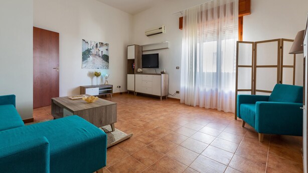 A modern living room with a sofa, a coffee table, a TV, and a kitchen area with a cabinet and an air conditioner. - 2253 Casa Jacopo (Mesagne)