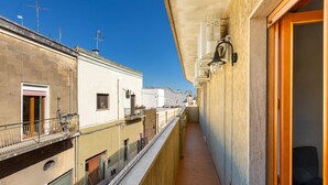 A narrow balcony with a view of adjacent buildings, a wooden door, and a small seating area. - 2253 Casa Jacopo (Mesagne)