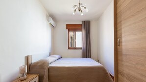 A bedroom with a bed, a nightstand, a lamp, a window with curtains, and a wooden door. - 2253 Casa Jacopo (Mesagne)