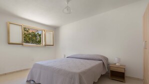 A bedroom with a bed, nightstand, and a window with a view of greenery.