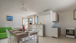 A modern kitchen with white cabinets, a dining table with chairs, a green sofa, and a painting on the wall.