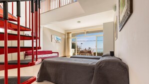 Une chambre avec un lit superposé, un escalier en colimaçon rouge, une grande fenêtre donnant sur un beau paysage et un tableau accroché au mur.