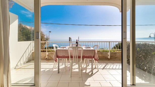 Un balcon avec une table et des chaises, une vue sur la mer et un mur en pierre.