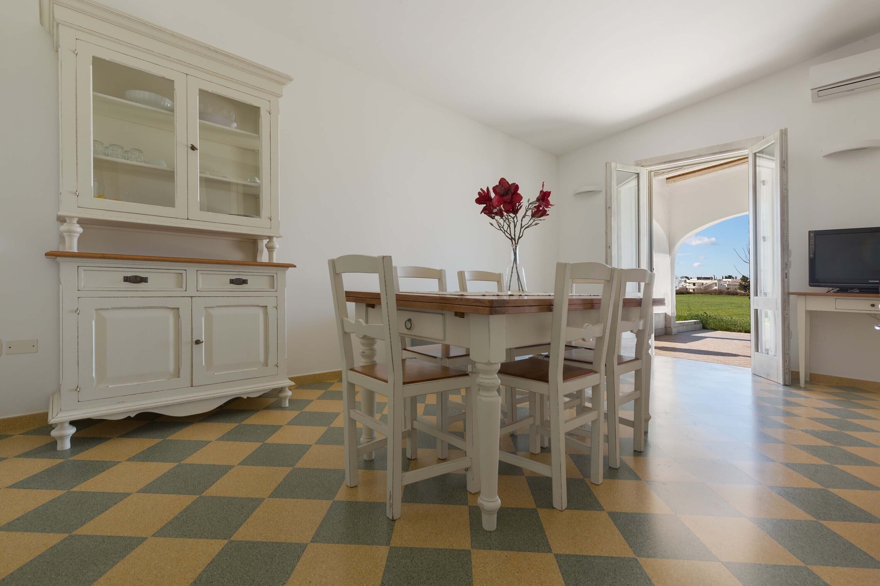 Ein Essbereich mit Schachbrettmuster-Boden, einem weißen Schrank mit Glastüren und Blick durch eine offene Tür.