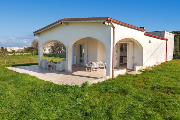 A white building with arched doorways and a covered patio area with outdoor seating.