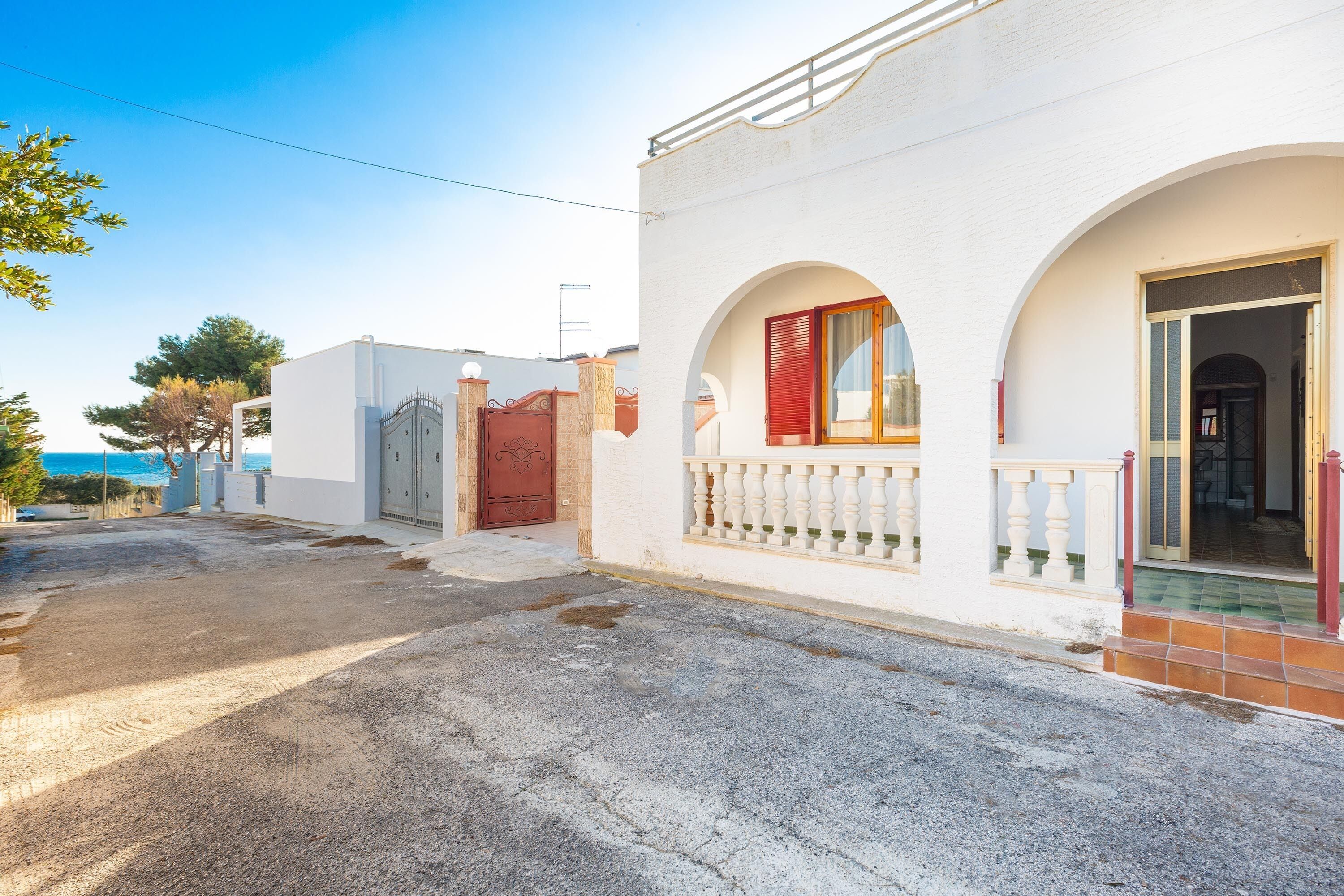 A white building with a gated entrance, a balcony, and a view of the sea.