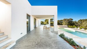 Ein modernes Haus mit überdachter Terrasse, Swimmingpool und Garten.