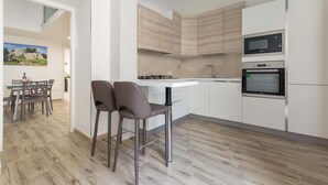 A modern kitchen with white cabinets, a built-in microwave, and an oven. There is a dining area with a table and chairs. - 2252 Suite 79 by Barbarhouse (Lecce)