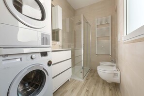 A compact, modern bathroom with a washing machine, a glass-enclosed shower, and a toilet.