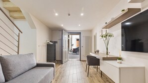 A modern living room with a grey sofa, a wooden floor, a TV mounted on the wall, and a staircase on the left. - 2252 Suite 79 by Barbarhouse (Lecce)