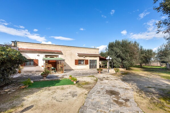 A house with a stone pathway leading to the entrance, surrounded by greenery and trees.