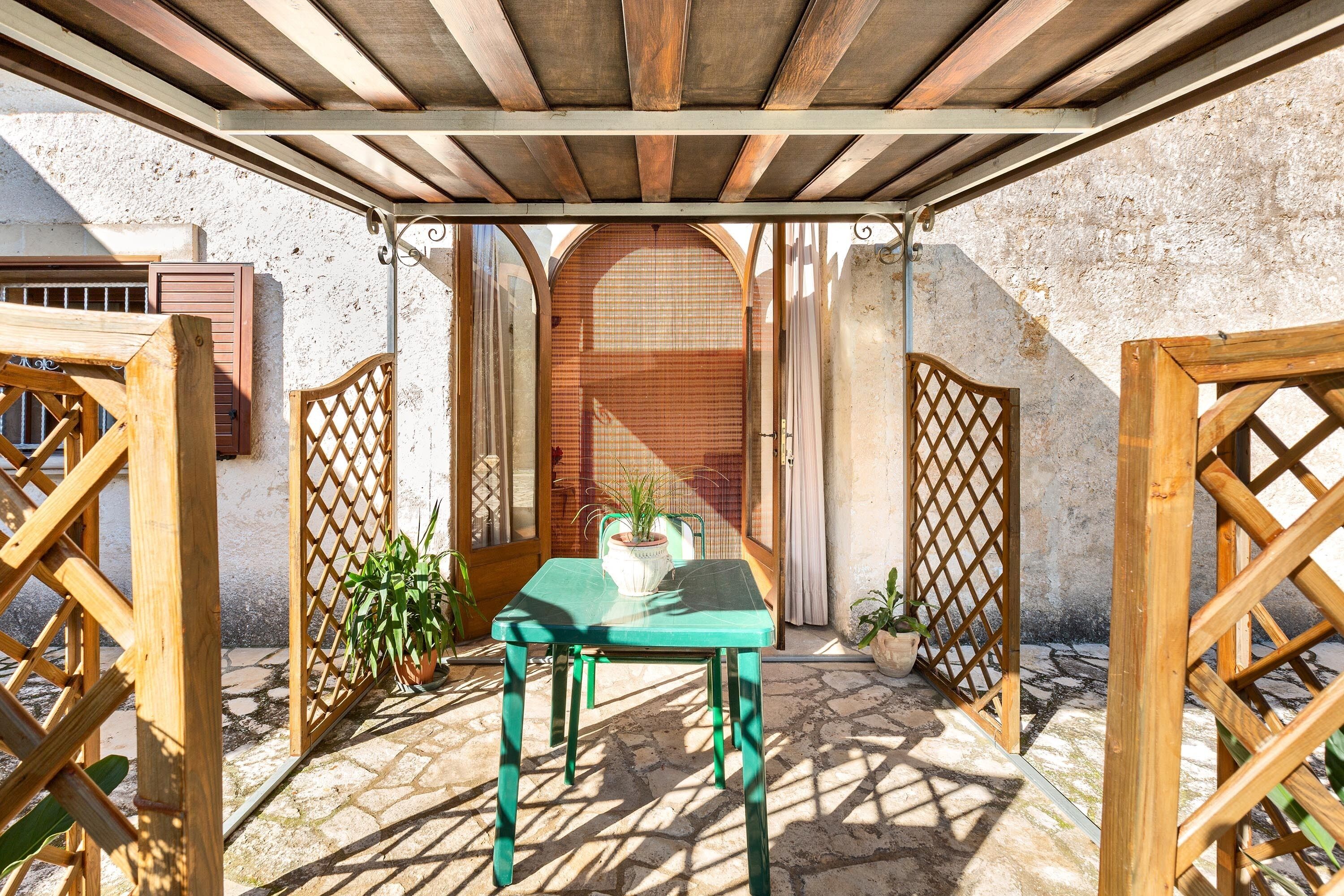 Une terrasse extérieure couverte, avec une table et des chaises en bois, entourée de portails en bois et de plantes en pot.
