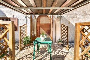 A covered outdoor patio with a wooden table and chairs, surrounded by wooden gates and potted plants.