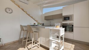A modern kitchen with white cabinets, a built-in oven, a microwave, and a small island with stools. - 2210 Villa Sergi by Perle di Puglia (Gagliano del Capo)