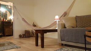 A cozy living room with a hammock, a wooden table, a lamp, and a sofa with patterned cushions. - Souterrainwohnung mit Großem Garten (Kassel)