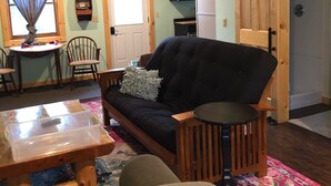 A cozy living room with a sofa, chairs, a table, and a kitchen area in the background.