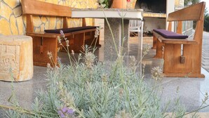 Un área de estar al aire libre con muros de piedra, un banco de madera, una mesa y una planta en maceta.