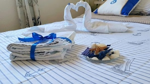 Una cama bien hecha con una colcha a rayas, una pila de toallas dobladas con un lazo azul, y un cuenco con caracolas decorativas.