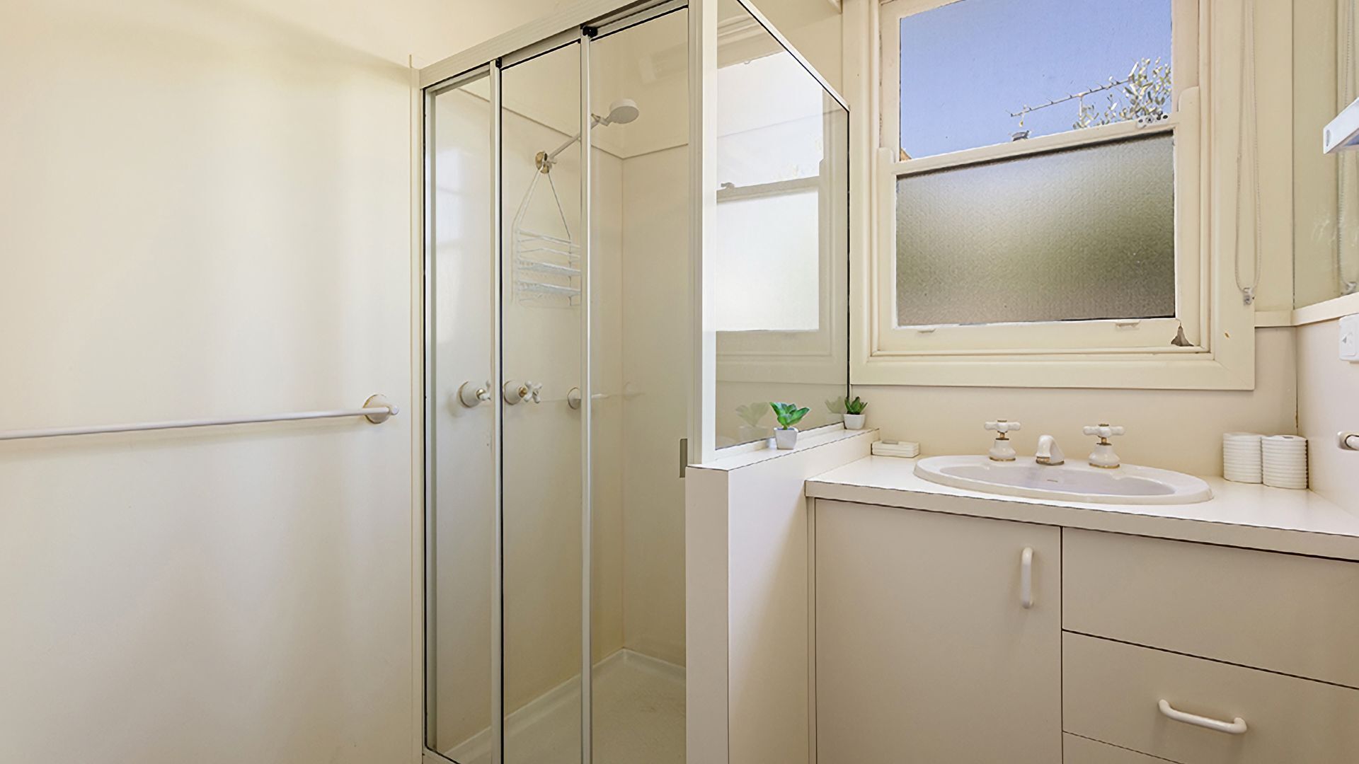 A bathroom with a glass shower enclosure, a sink with a mirror above, and a window.