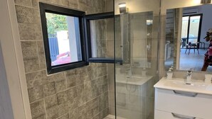 Un baño moderno con cabina de ducha de vidrio, un lavabo blanco y una ventana con vistas al exterior.