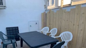 Un patio con una mesa negra y sillas de plástico blanco, un cerco de madera y una puerta blanca.