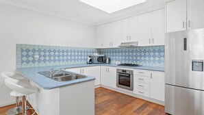 A modern kitchen with white cabinets, a blue and white tiled backsplash, stainless steel appliances, and a wooden floor. - Esplanade Townhouse 4-209 Only 50m to Beach (Torquay)