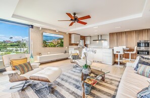 Ein modernes Wohnzimmer mit großem Fenster, Deckenventilator und Blick auf eine Stadtlandschaft.