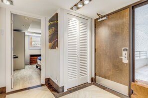A hallway with a wooden door, a white door with blinds, and a bed in the background.