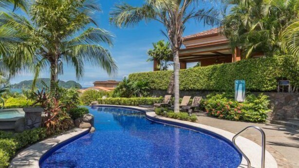 A pool surrounded by lush greenery and palm trees, with a stone structure and lounge chairs. - Ocean View, Modern Luxury w/Jacuzzi & access to all amenities! (Puntarenas)