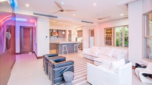 A modern living room with a white sofa, a coffee table, and a seating area with cushioned chairs. There is a kitchen in the background with a bar and stools. - Ocean View, Modern Luxury w/Jacuzzi & access to all amenities! (Puntarenas)