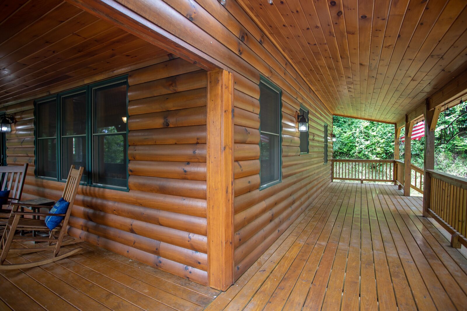 Una cabaña de troncos con terraza de madera, sillas mecedoras y porche cubierto.