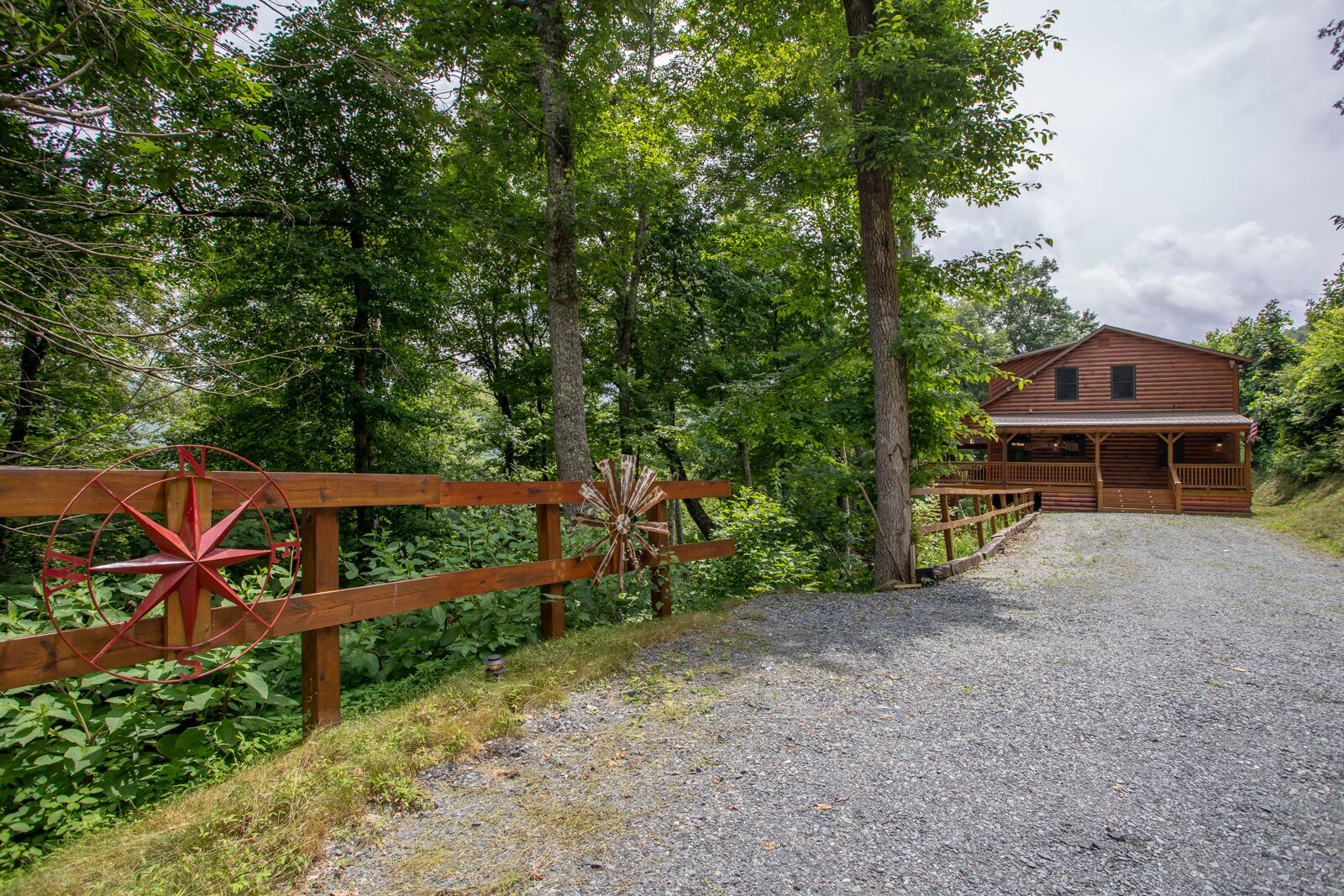 A wooden cabin with a porch, surrounded by trees and a gravel path leading to it.