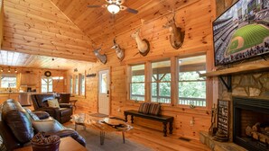 A cozy cabin interior with wooden walls, a fireplace, leather furniture, and mounted deer heads. - Spacious Log Home with EV Charger (Vilas)