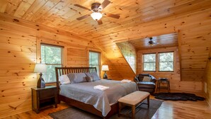 A cozy wooden cabin bedroom with a bed, a chair, a small table, and a ceiling fan. - Spacious Log Home with EV Charger (Vilas)
