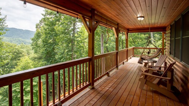 A wooden deck with a railing, a hanging light fixture, and a view of a forested landscape. - Spacious Log Home with EV Charger (Vilas)