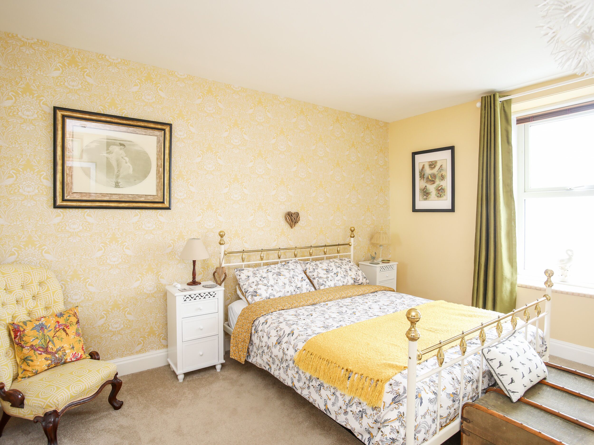 Een slaapkamer met een bed, nachtkastjes, een stoel en een raam met gordijnen.