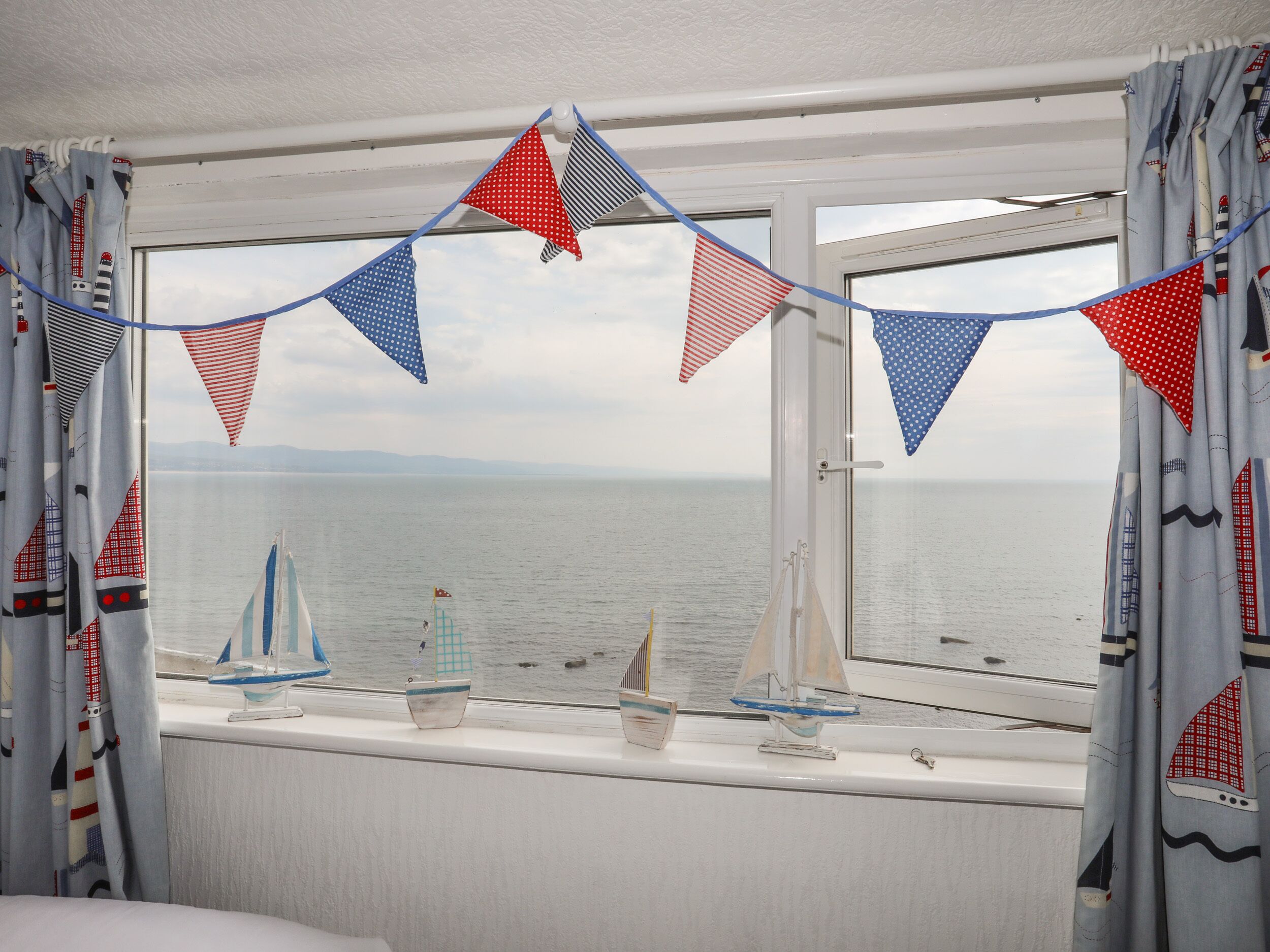 A room with a large window overlooking the sea, featuring a view of sailboats and a decorative string of triangular flags.
