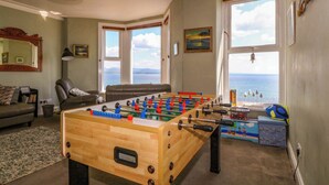 Un salon chaleureux avec une table de baby-foot, un canapé, une table basse et une vue sur la mer grâce à de grandes fenêtres.