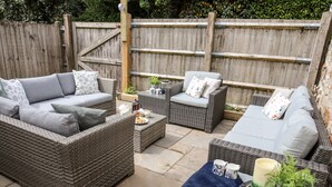 Un espace patio aménagé avec des meubles en osier, notamment des canapés et une table agrémentée d’un service à thé et de plantes.