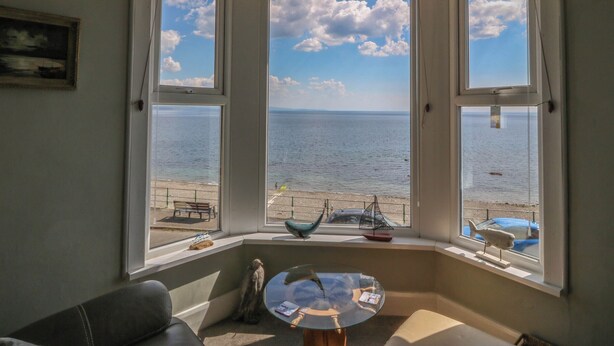 Une pièce avec vue sur la mer, grâce à de grandes fenêtres, une petite table et un banc à l’extérieur.