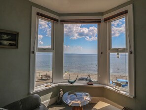 Een kamer met uitzicht op de zee, grote ramen, een kleine tafel en een bankje buiten.