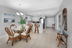 A modern kitchen with white cabinets, a central island, and a dining area with wicker chairs and a glass table.
